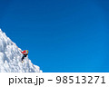 A climber in a red suit climbs an icy white mountain 98513271