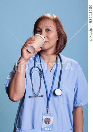 Senior asian nurse holding beverage cup drinking coffee before checkup visit appointment, health care service. Physician medical assistant working at patient disease expertise. Medicine concept 98513586
