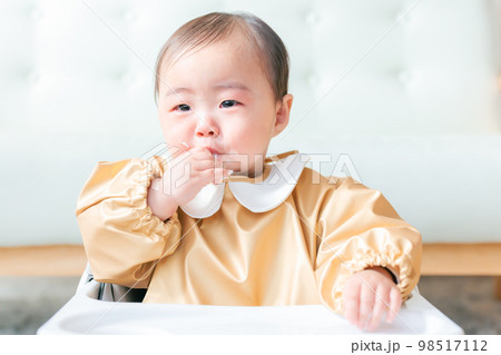 泣きながら離乳食を食べる手づかみ食べの赤ちゃん 98517112