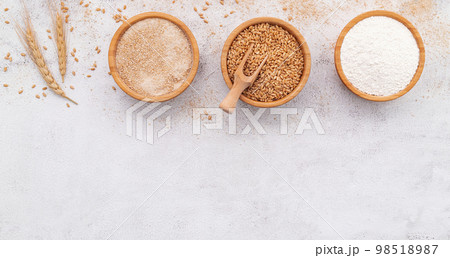 Wheat grains , brown wheat flour and white wheat flour in wooden bowl set up on white concrete background. 98518987