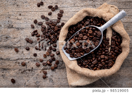 Background of dark roasted coffee beans with scoops setup on wooden background with copy space. 98519005