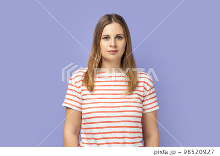 Portrait of serious confident blond woman wearing striped T-shirt standing looking at camera with attentive look, being strict and bossy. Indoor studio shot isolated on purple background. Portrait of serious confident blond woman wearing striped T-shirt standing looking at camera with attentive look, being strict and bossy. Indoor studio shot isolated on purple background. 98520927