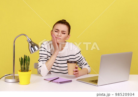 Unhappy woman office worker touching cheek with fingers feeling unpleasant toothache after drinking hot coffee, dentistry problems. Indoor studio studio shot isolated on yellow background. 98520934