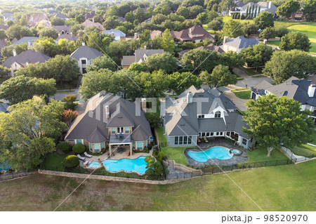 Aerial drone view of luxury mansions with swimming pools surrounded by green grass and trees in the summertime. Aerial drone view of luxury mansions with swimming pools surrounded by green grass and trees in the summertime. 98520970