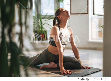 Young fit woman practice yoga doing asana in light yoga studio with green house plant 98521676