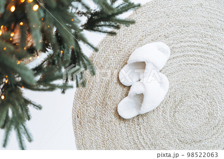 Cozy fluffy slippers on natural rug near Christmas tree Cozy fluffy slippers on natural rug near Christmas tree 98522063