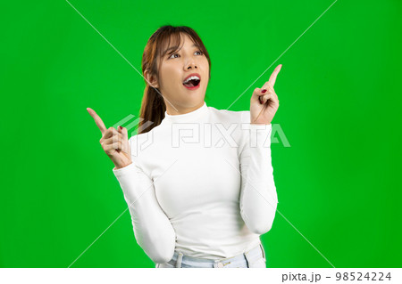 Young Asian woman wearing white shirt pointing at something on green screen. Young Asian woman wearing white shirt pointing at something on green screen. 98524224