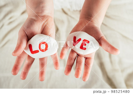 Hands of little girl hold two white smooth stones with syllables lo and ve painted red on white cloth background. Love Hands of little girl hold two white smooth stones with syllables lo and ve painted red on white cloth background. Love 98525480