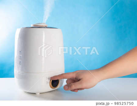 A man sets the percentage of humidity in a room on a humidifier, blue background. Copy space for text A man sets the percentage of humidity in a room on a humidifier, blue background. Copy space for text 98525750