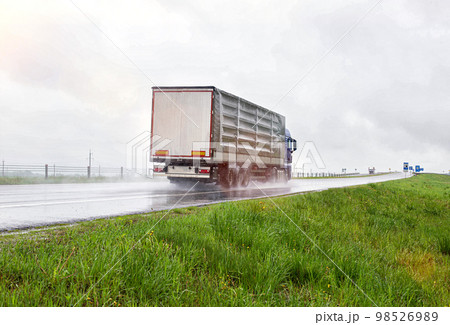 A truck with a semi-trailer transports cargo in rainy weather on a slippery road. Automobile cargo transportation. Copy space for text 98526989
