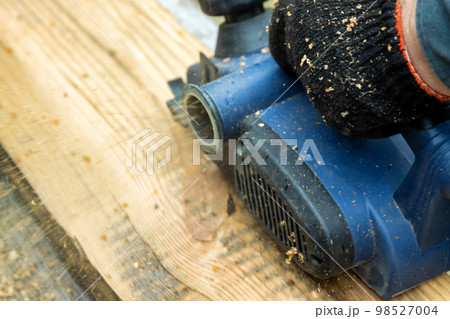 A male carpenter plans boards with an electric planer to make a bench. Carpentry, industry. Woodworker 98527004