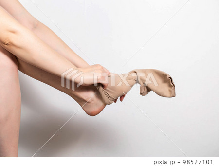 A woman puts on compression stockings for legs with varicose veins. Pain and swelling in the legs, phlebology. White background, close-up. Bloodstream 98527101