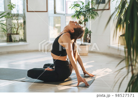 Young fit woman practice yoga doing asana in light yoga studio with green house plant 98527571