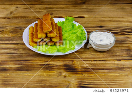 Fried fish fingers on a plate with lettuce and tartar sauce on wooden table 98528971