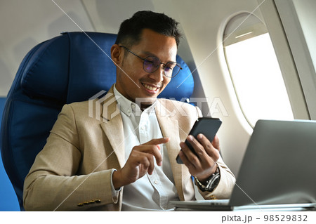 Millennial businessman passenger sitting on airplane cabin and using smart phone. Business or travel abroad concept 98529832