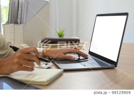 Cropped view of female employee hand typing on laptop computer and writing records to daily planner 98529909