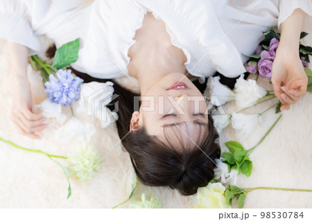 寝転がって花に囲まれる若い女性の顔のアップ 寝転がって花に囲まれる若い女性の顔のアップ 98530784