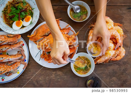 Top view Steamed Crabs and Shrimps set on the vintage wooden table with the the Asian hand picks up seafood sauce above of it before they eat. Top view Steamed Crabs and Shrimps set on the vintage wooden table with the the Asian hand picks up seafood sauce above of it before they eat. 98530993
