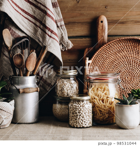 Eco-friendly kitchen concept: Kitchen cooking utensils, house plants and cooking ingredients in glass jars against rustic kitchen wall 98531044