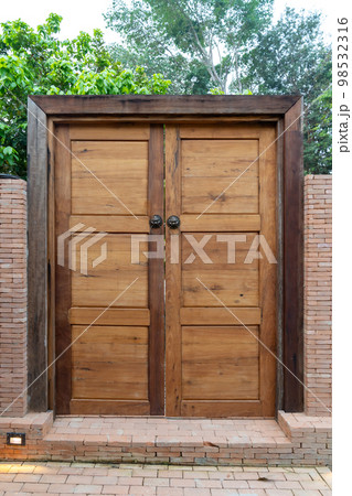 Wooden door and wood frame with the Bronze Knocked Chinese Lion head style on it. This is middle of the brick wall in the garden environment 98532316