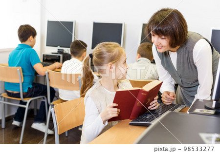 Woman teacher helping tween girl in computer class 98533277