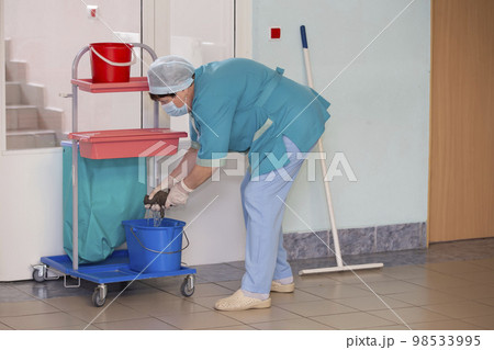 An adult female cleaner in uniform cleans the corridor of the hospital. 98533995