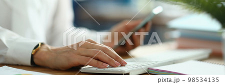 Female hands hold smartphone and work on laptop keyboard 98534135