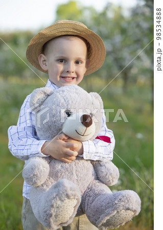 A happy child in a blooming garden holds a toy bear. 98534888