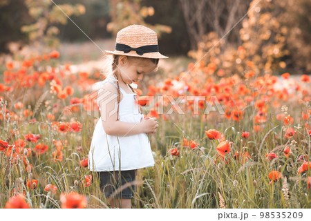 Cute funny baby girl 2-3 year old wear straw hat and white summer dress over flower meadow background. Kid laughing outdoors over nature 98535209