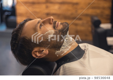 Headshot of a man sitting at the barbershop before shaving Headshot of a man sitting at the barbershop before shaving 98536648