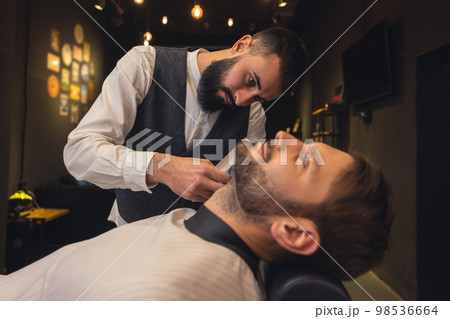 Professional barber carefully trimming the clients beard 98536664