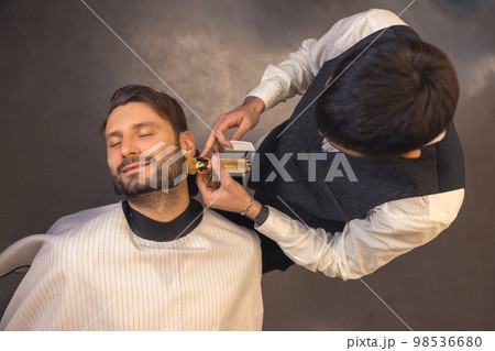 Barber trimming the clients beard 98536680
