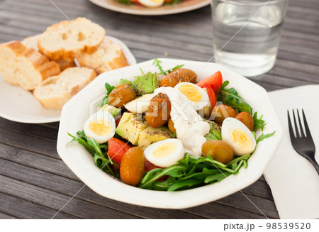 dish of fresh vegetables arugula, avocado, cherry tomatoes with olives and quail eggs on dining table dish of fresh vegetables arugula, avocado, cherry tomatoes with olives and quail eggs on dining table 98539520