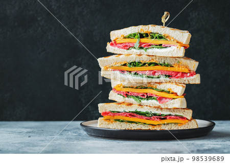 Big homemade sandwich with sausage, cheese and arugula on a dark concrete background 98539689