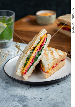 Two homemade sandwiches with sausage, cheese and arugula on a light concrete background Two homemade sandwiches with sausage, cheese and arugula on a light concrete background 98539752
