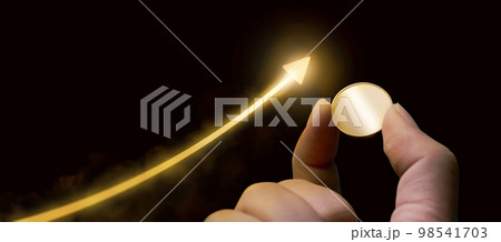A hand holding gold coin and growing golden arrow with dark black background 98541703