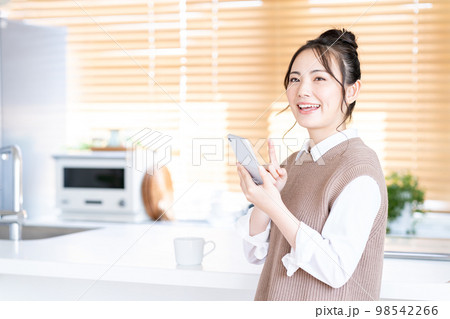 キッチンでスマホを操作する若い女性。 キッチンでスマホを操作する若い女性。 98542266