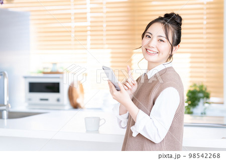 キッチンでスマホを操作する若い女性。 98542268