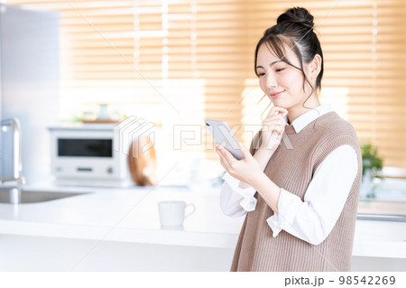 キッチンでスマホを操作する若い女性。 98542269