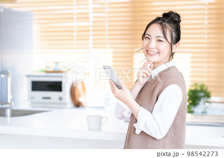 キッチンでスマホを操作する若い女性。 98542273