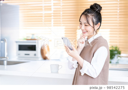 キッチンでスマホを操作する若い女性。 98542275