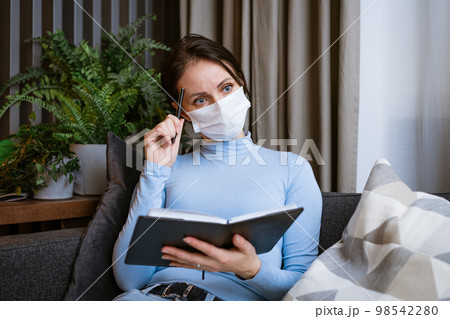 Woman in protective mask on the couch with notepad in hand 98542280