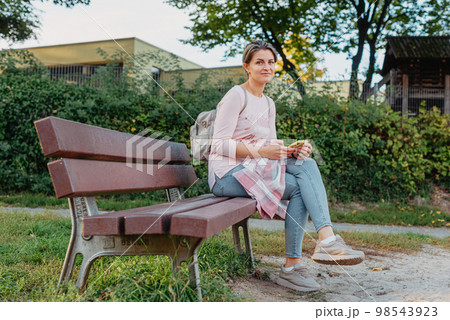 Girl enjoying city view from a bench in sunset or sunrise time. Beautiful blond-haired pretty girl in summer green park against sunset beams. Lonely woman sitting alone moments sunset. On Blurred Girl enjoying city view from a bench in sunset or sunrise time. Beautiful blond-haired pretty girl in summer green park against sunset beams. Lonely woman sitting alone moments sunset. On Blurred 98543923