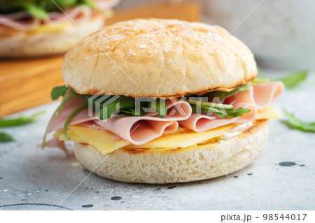 Two homemade sandwiches with ham, cheese and arugula on a concrete table. 98544017