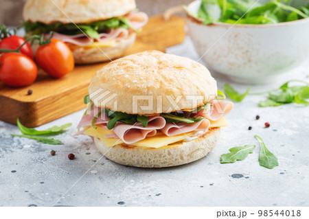 Two homemade sandwiches with ham, cheese and arugula on a concrete table. Two homemade sandwiches with ham, cheese and arugula on a concrete table. 98544018