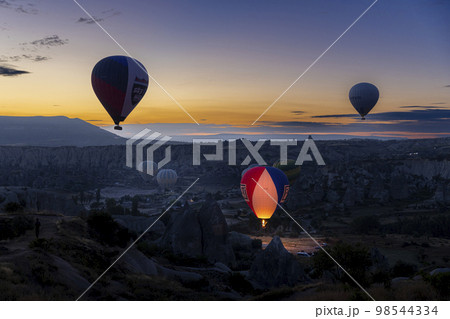 Hot air balloons fly at dawn over the hills of Goreme. 98544334