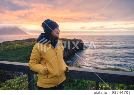 Young asian woman standing and watching puffin bird on the cliff in Borgarfjordur Eystri 98544702