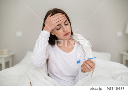 Unhappy woman touching forehead and holding thermometer 98546483