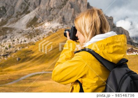 Woman takes photos of scenic Passo Giau pass. Traveler with backpack uses camera to capture Italian Alps Woman takes photos of scenic Passo Giau pass. Traveler with backpack uses camera to capture Italian Alps 98546736