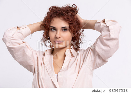 The girl corrects her curly hair with two hands. European. 98547538